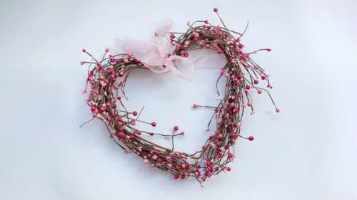 A heart-shaped wreath made of soft pink flowers and green leaves isolated on a white... wallpaper