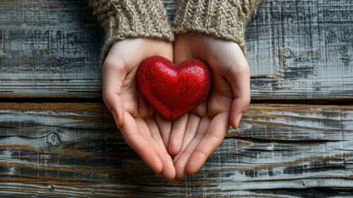 Two hands holding a red heart on a rustic wooden surface for Valentine's Day. free background