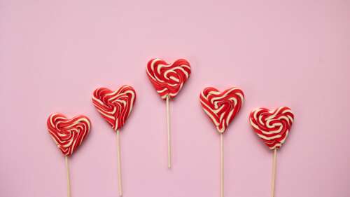 An assortment of pastel pink candies and red heart-shaped lollipops arranged aesthetically. high definition wallpaper