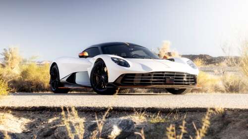 A sleek white Aston Martin Valhalla supercar driving through a bright, expansive... free background