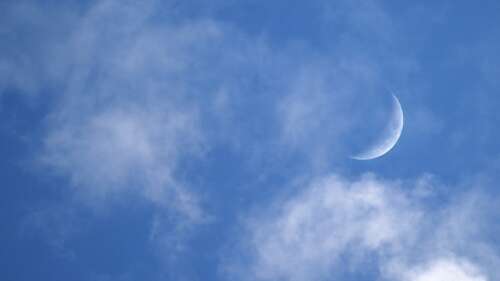 A luminous crescent moon shining through soft clouds in a deep blue night sky. high definition wallpaper