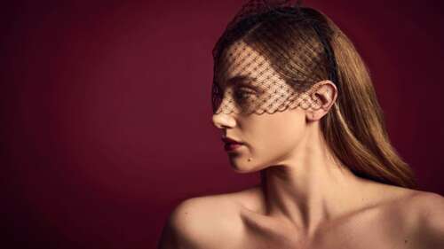 A professional portrait of Lili Reinhart set against a vibrant, solid red background...