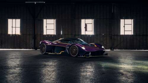 A purple Aston Martin Valkyrie hypercar parked inside a contemporary industrial hangar. free wallpaper