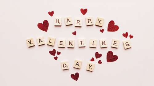 Wooden Scrabble tiles spelling 'Happy Valentine's Day' decorated with small red hearts... free background