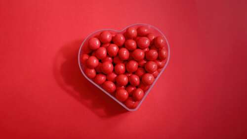 A heart shape made of various colorful sugar candies set against a bright red background. free wallpaper