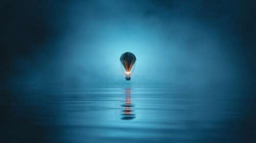 A hot air balloon floating in a misty and foggy night sky with reflections on a still... wallpaper