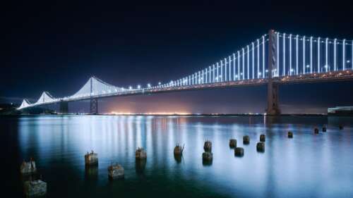 San Francisco-Oakland Bay Bridge at night with bright lights reflecting on the water... free wallpaper