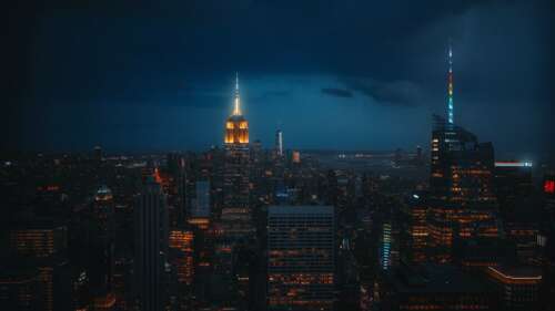 A dark, cinematic night view of the New York City skyline featuring the illuminated... high definition wallpaper
