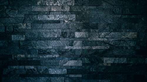 Close-up of a dark, textured brick wall in a low-light setting with deep shadows. wallpaper