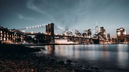 A nighttime view of the Brooklyn Bridge in New York City featuring a crescent moon... wallpaper