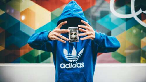A man wearing an Adidas hoodie surrounded by playing cards in a dark casino-themed... wallpaper
