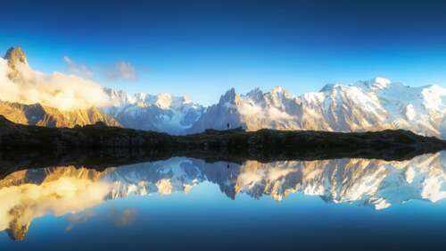 Snow-capped Alps mountains reflecting in a clear lake under a vibrant blue sky. wallpaper