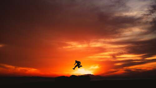 A silhouette of a man jumping in the Hisma Desert, Saudi Arabia, under a colorful... wallpaper