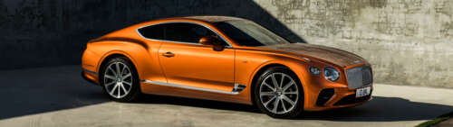 A glossy orange Bentley Continental GT luxury car parked in a scenic setting free hd wallpapers