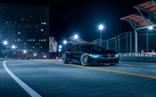 A sleek BMW i8 supercar parked on a dark street at night, featuring glowing headlights...