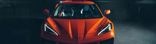 A bright orange Chevrolet Corvette C8 sports car highlighting its sleek aerodynamic... Dual UHD desktop wallpaper