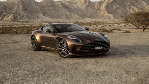 A high-resolution shot of an Aston Martin DB12 driving through golden desert sand... free desktop wallpaper