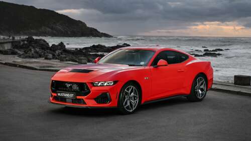 A vibrant red 2024 Ford Mustang GT parked on the sand with ocean waves in the background. wallpaper
