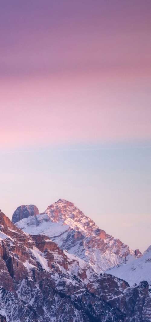 A panoramic view of snow-covered mountains at sunset with a colorful gradient sky... wallpaper