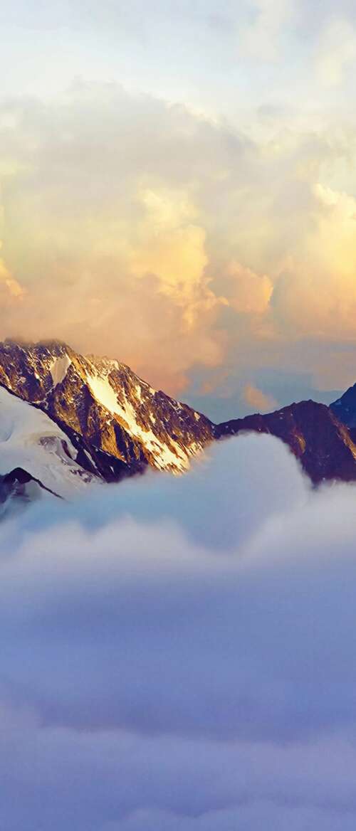 Snow-covered Alps mountain range partially obscured by fog and clouds. download free wallpaper for phone
