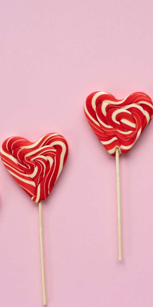 Assorted heart-shaped candies and lollipops in pastel pink and red. wallpaper