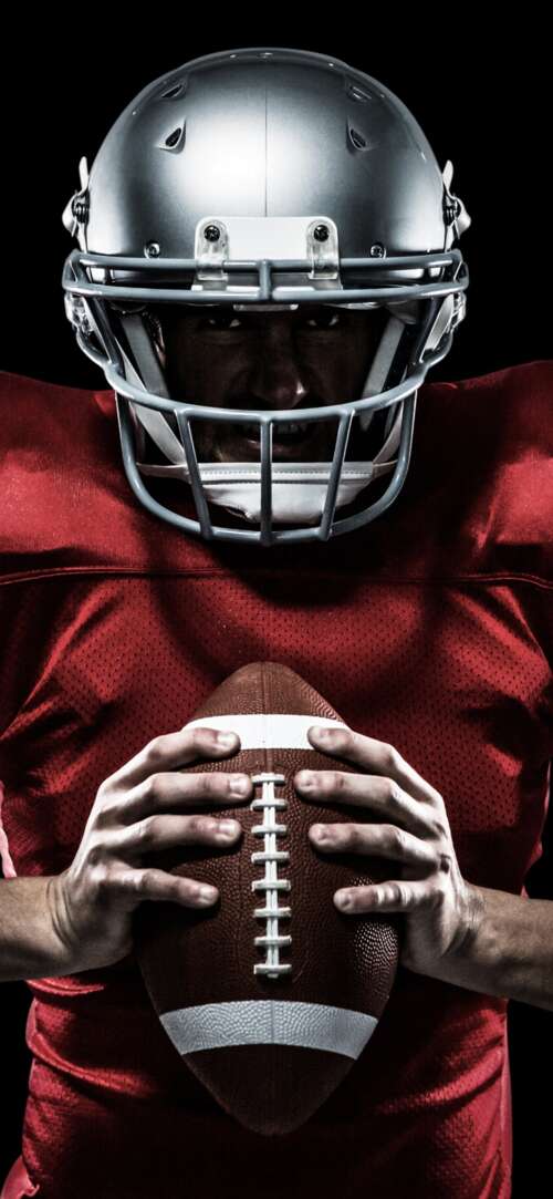 Close-up portrait of an American football player wearing a helmet and jersey against... wallpaper
