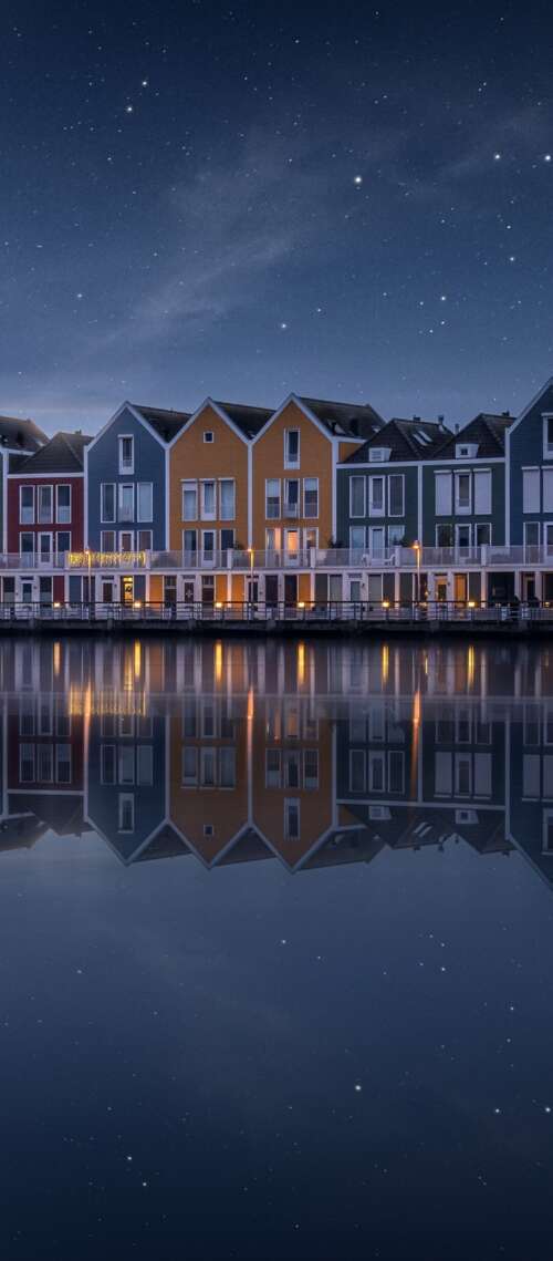 A colorful wooden house by a lake in the Netherlands under a starry evening sky with... free wallpaper