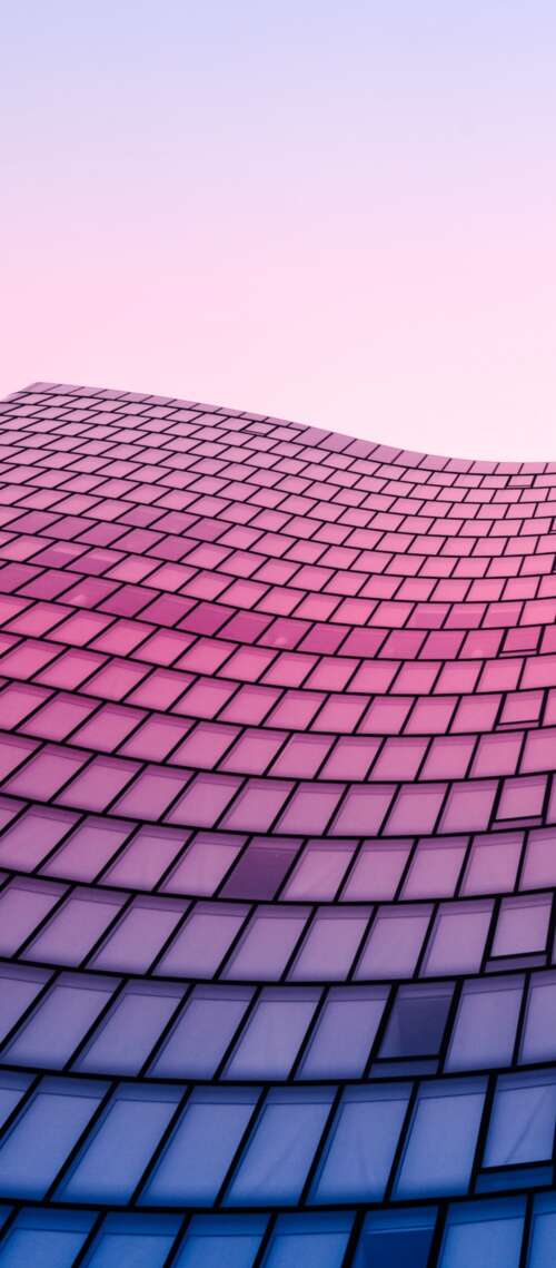 Low angle shot looking up at a vibrant glass skyscraper with geometric patterns against... free wallpaper