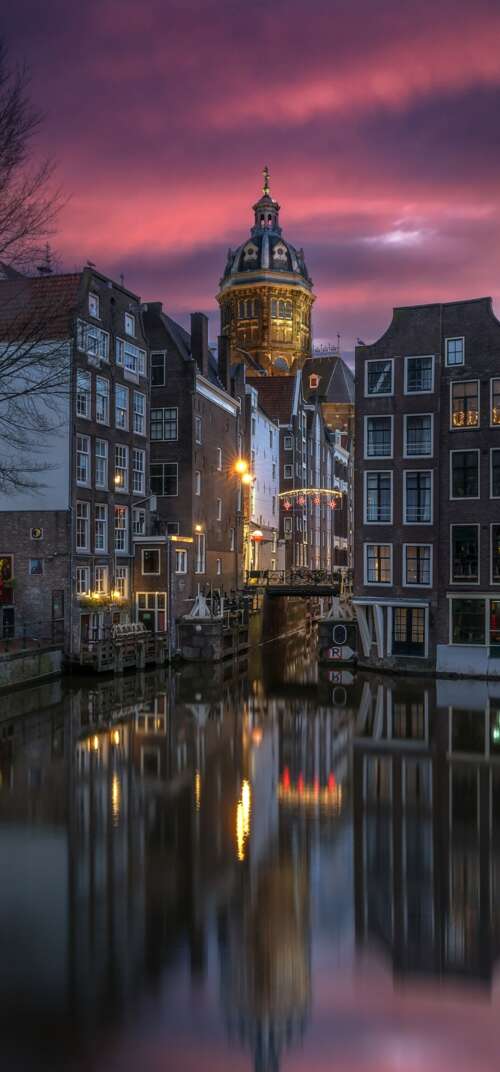A scenic night view of Amsterdam canals with sunset reflections on the water and... mobile wallpaper