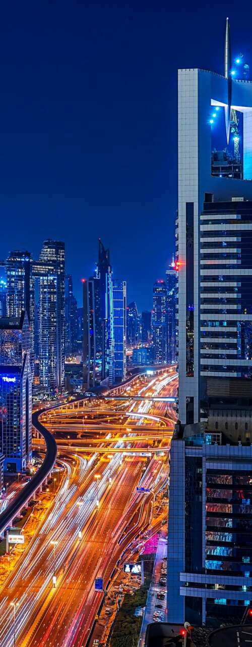A long exposure night view of the Dubai skyline featuring glowing skyscrapers and... wallpaper