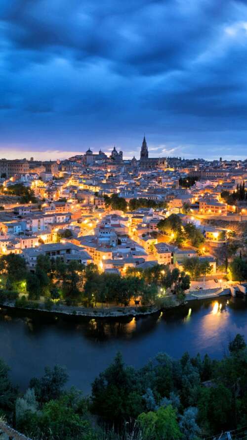 A wide panoramic view of a Spanish cityscape at night, featuring glowing urban lights... high definition wallpaper