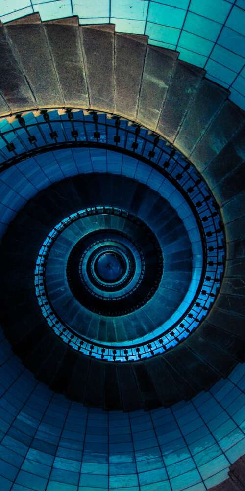 Looking up a blue spiral staircase inside a lighthouse in France, showcasing a geometric... free wallpaper