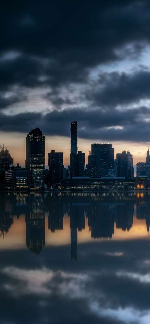The Manhattan skyline and skyscrapers reflected in the Hudson River during a beautiful... wallpaper
