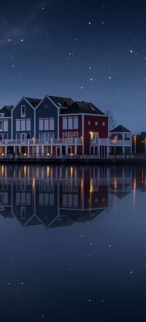 A colorful wooden house by a lake in the Netherlands under a starry evening sky with... wallpaper