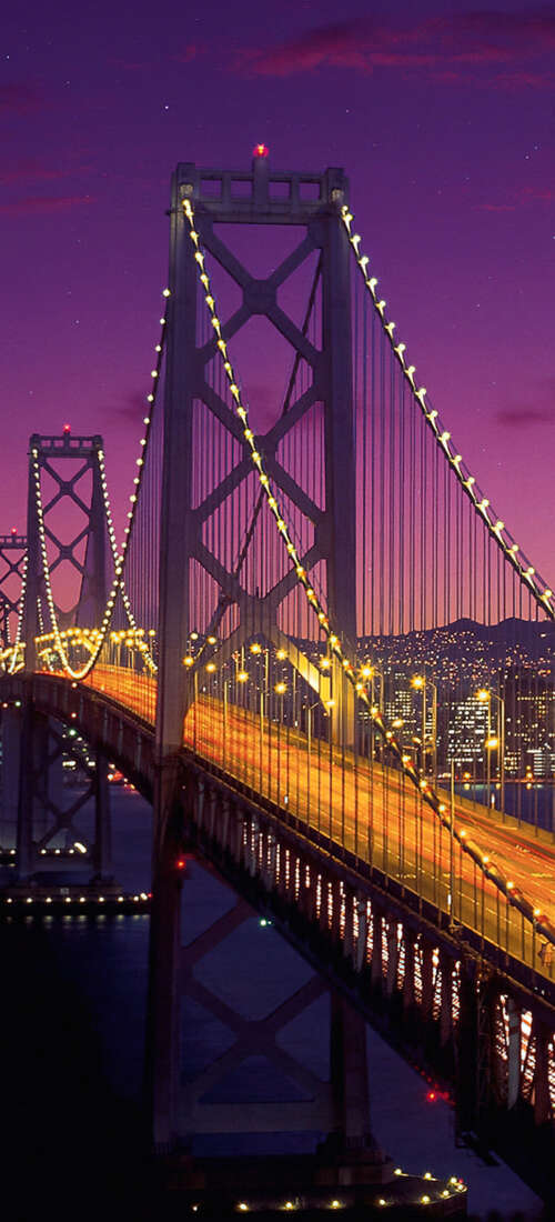 A long exposure photograph of the San Francisco-Oakland Bay Bridge under a deep purple... wallpaper