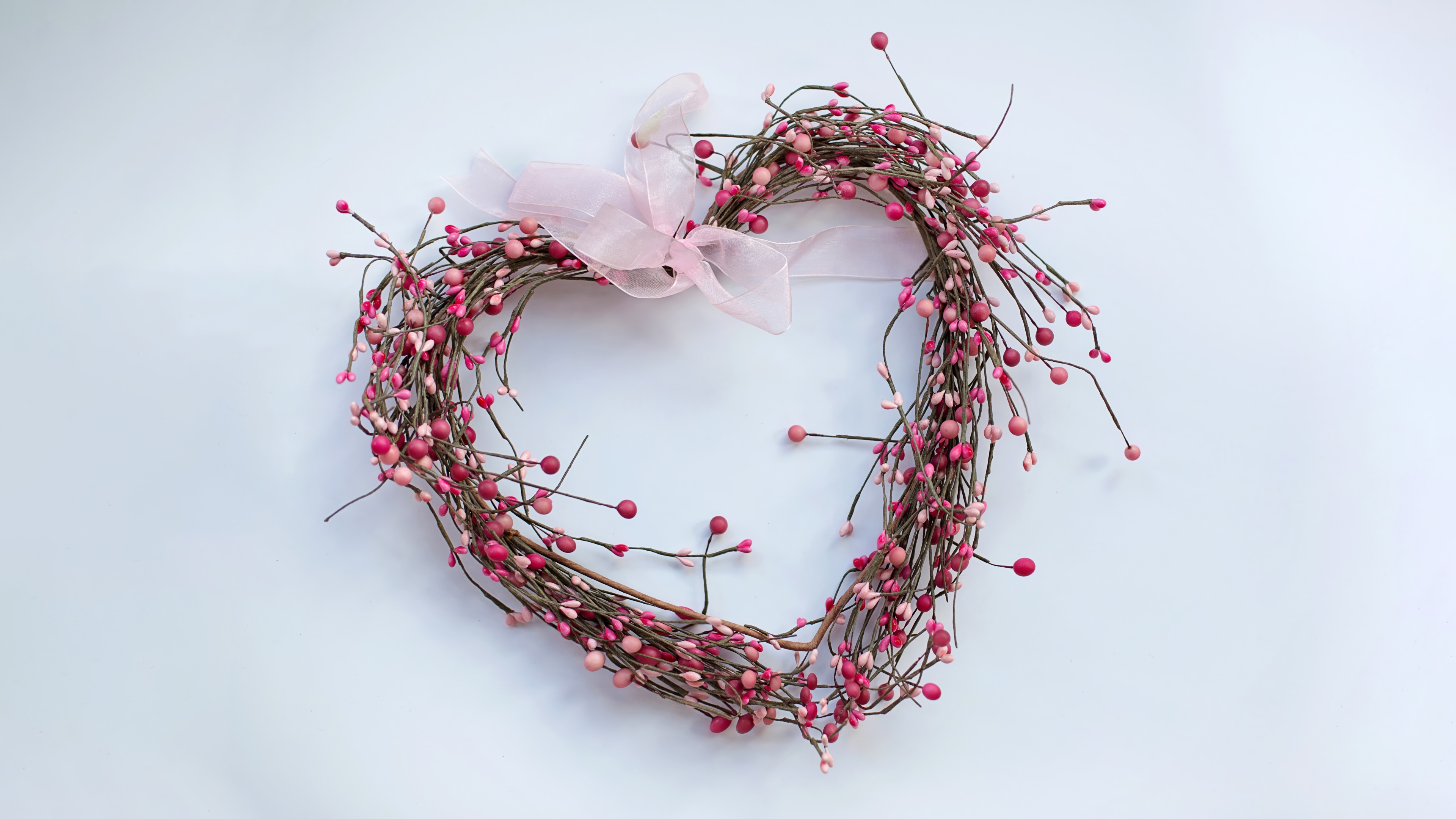 A heart-shaped wreath made of soft pink flowers and green leaves isolated on a white background.