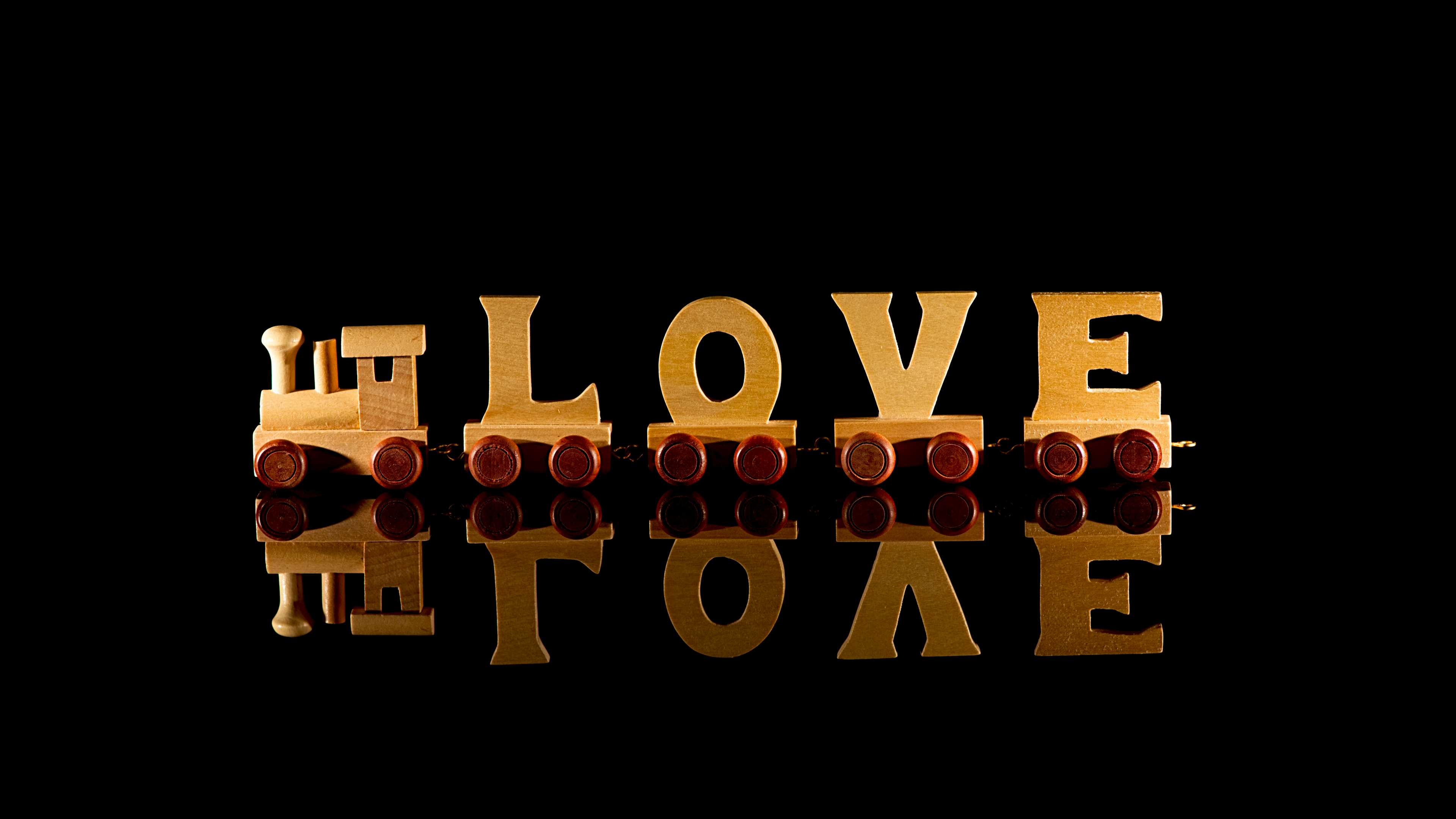 The word 'Love' rendered in 3D wooden letters on a glossy black surface with reflections.