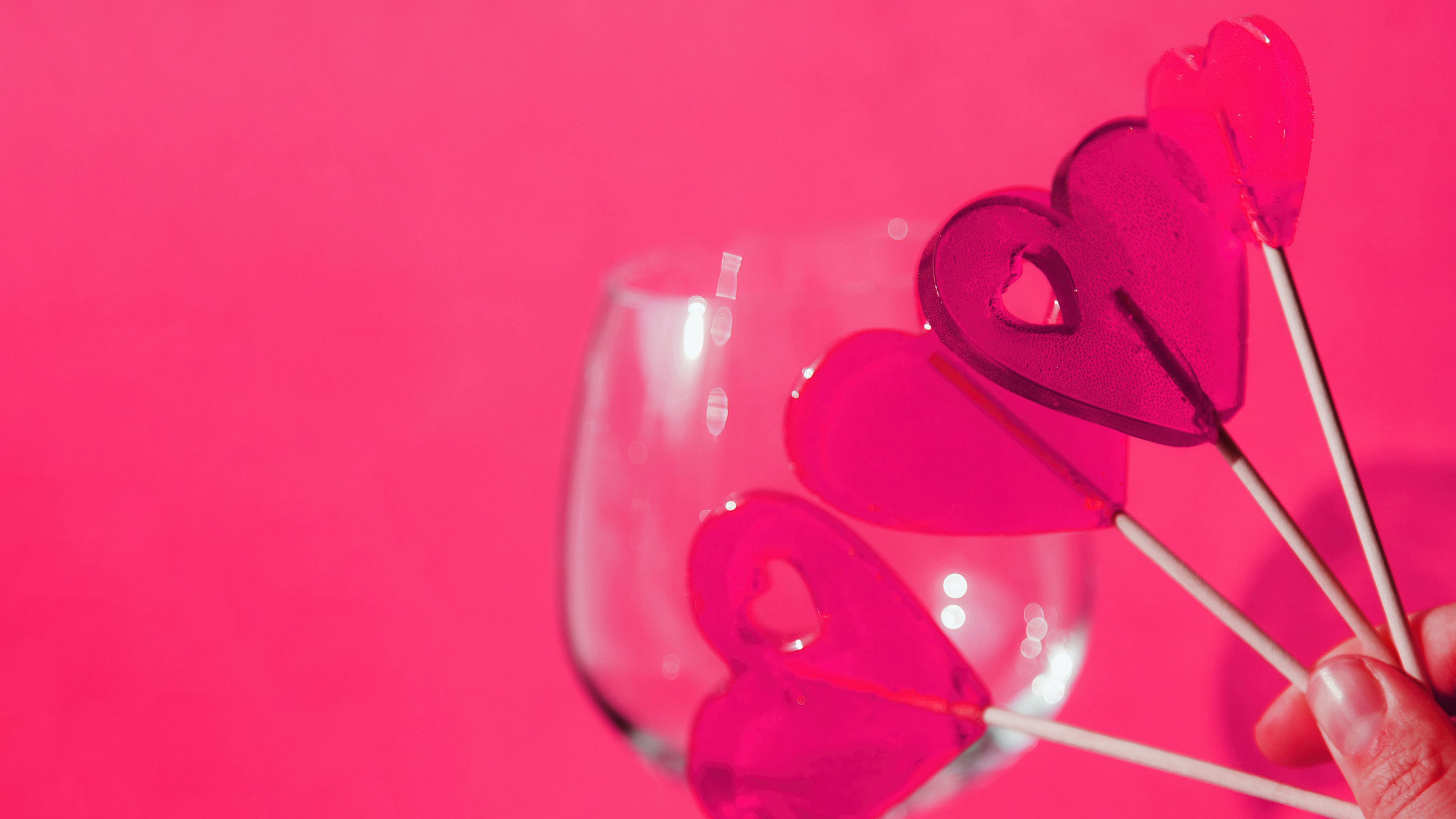 A pink lollipop surrounded by several floating pink hearts on a solid pink background.