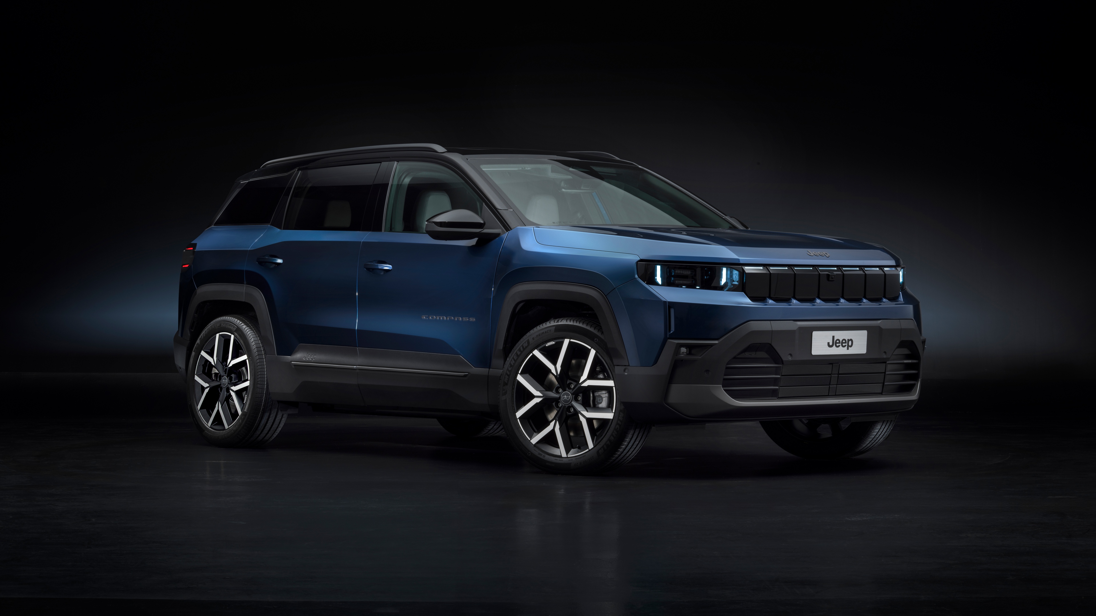 A sleek and modern 2025 Jeep Compass e electric SUV presented in a dark, cinematic setting.
