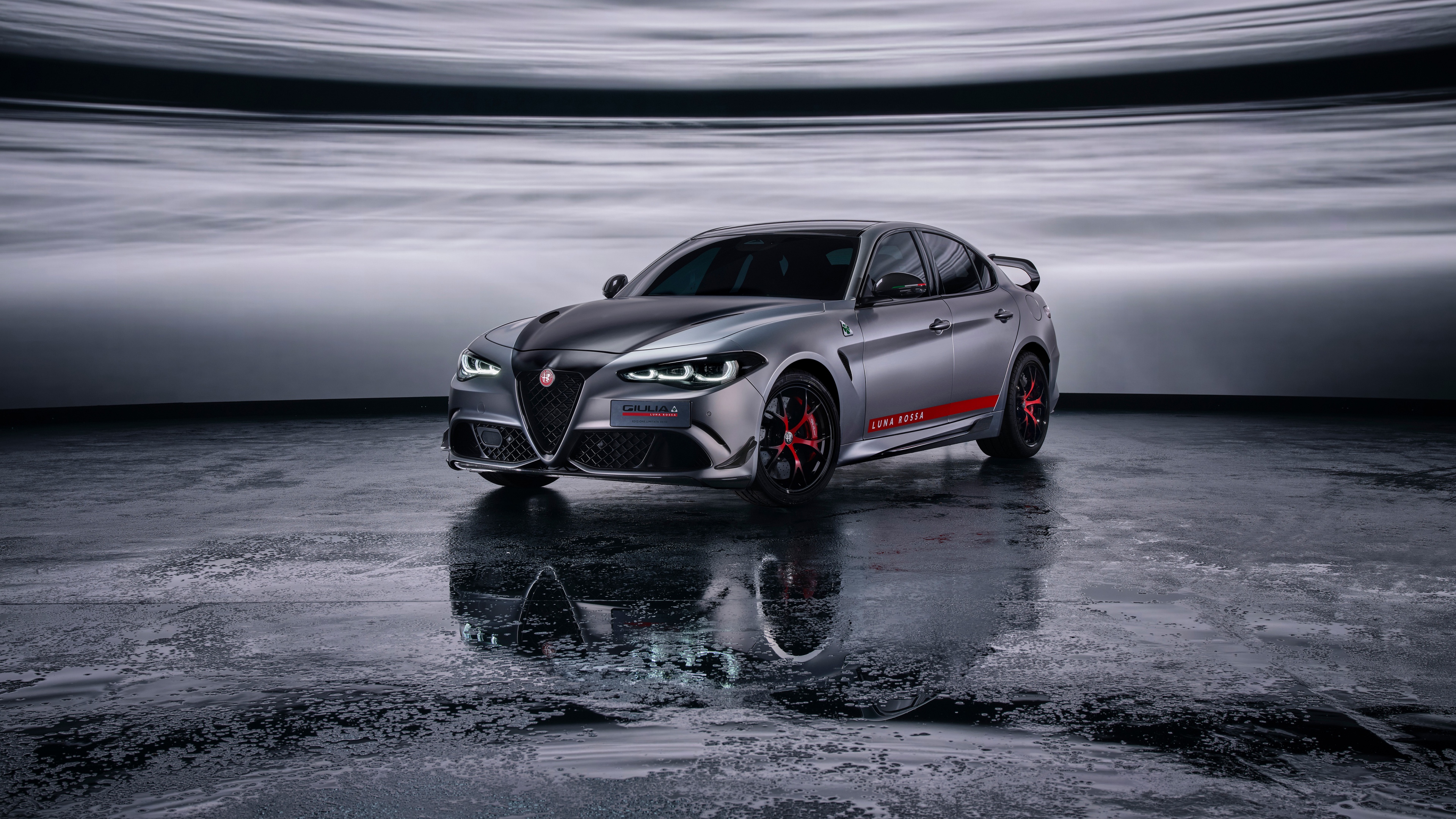 A sleek Alfa Romeo Giulia Quadrifoglio sports sedan positioned against a dark, moody background highlighting its aerodynamic design.