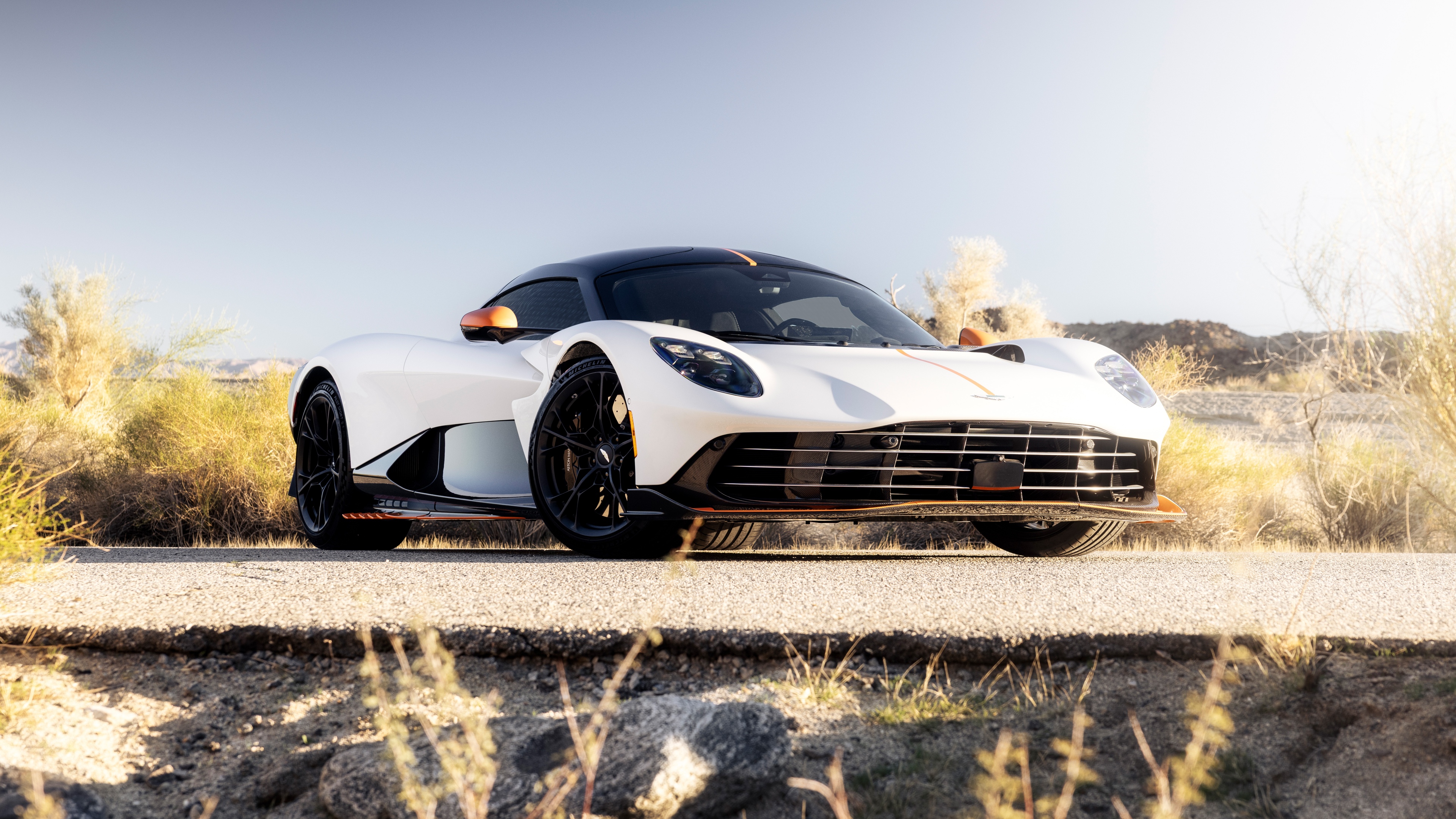A sleek white Aston Martin Valhalla supercar driving through a bright, expansive desert landscape.