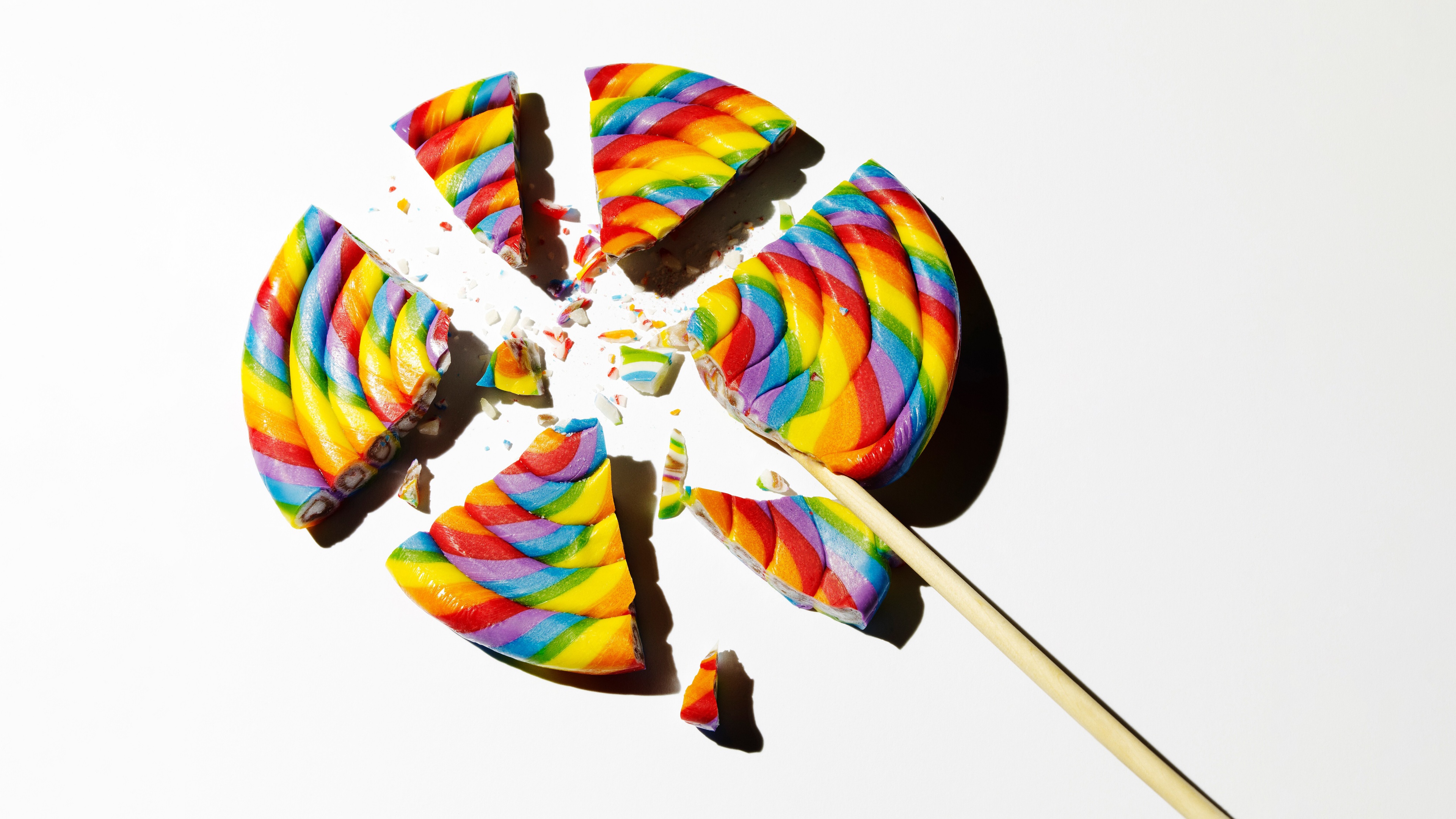 A broken, colorful rainbow spiral lollipop on a plain white background.