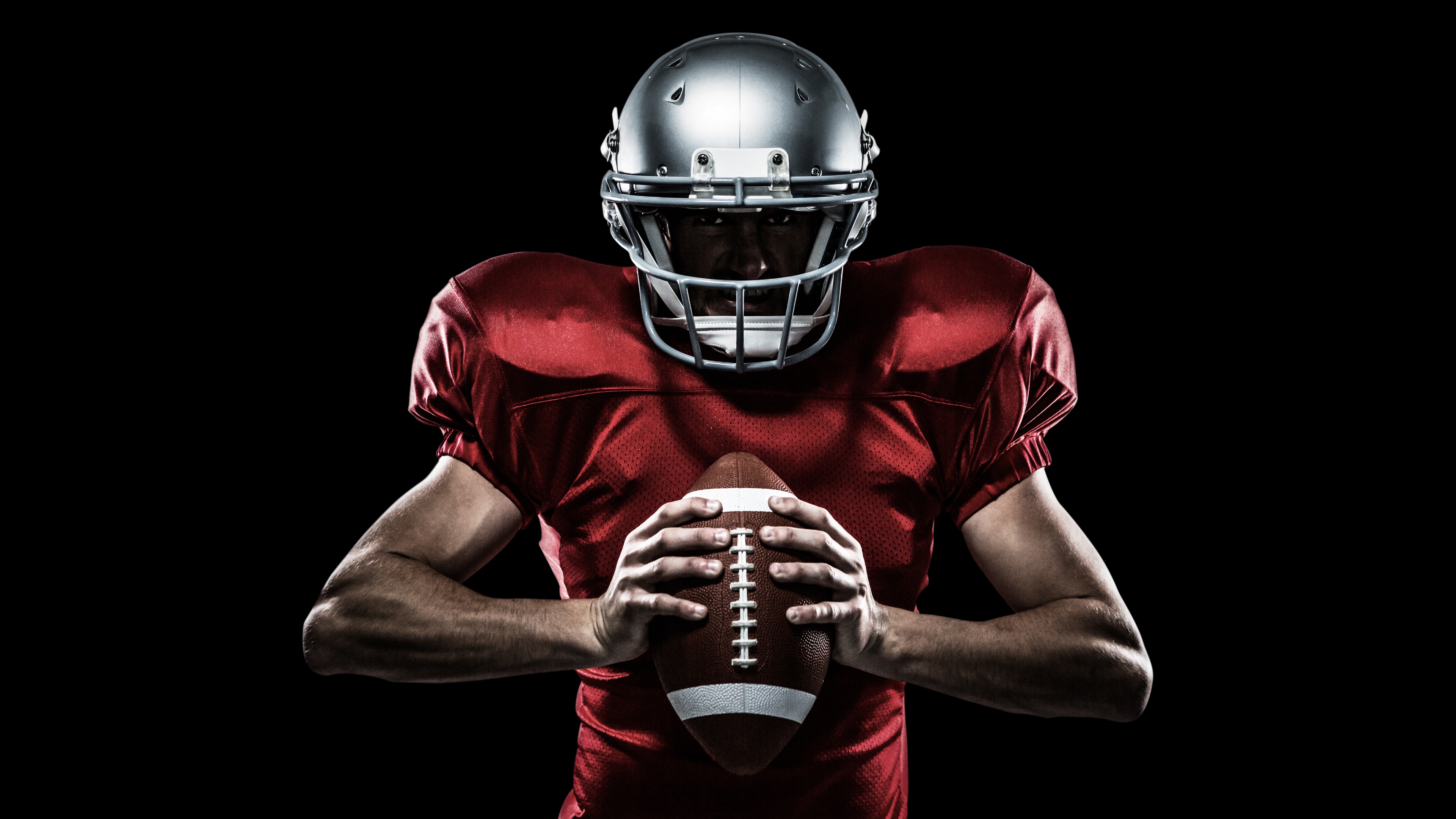 A close-up, dramatic shot of an American football player wearing a helmet and jersey against a black background.