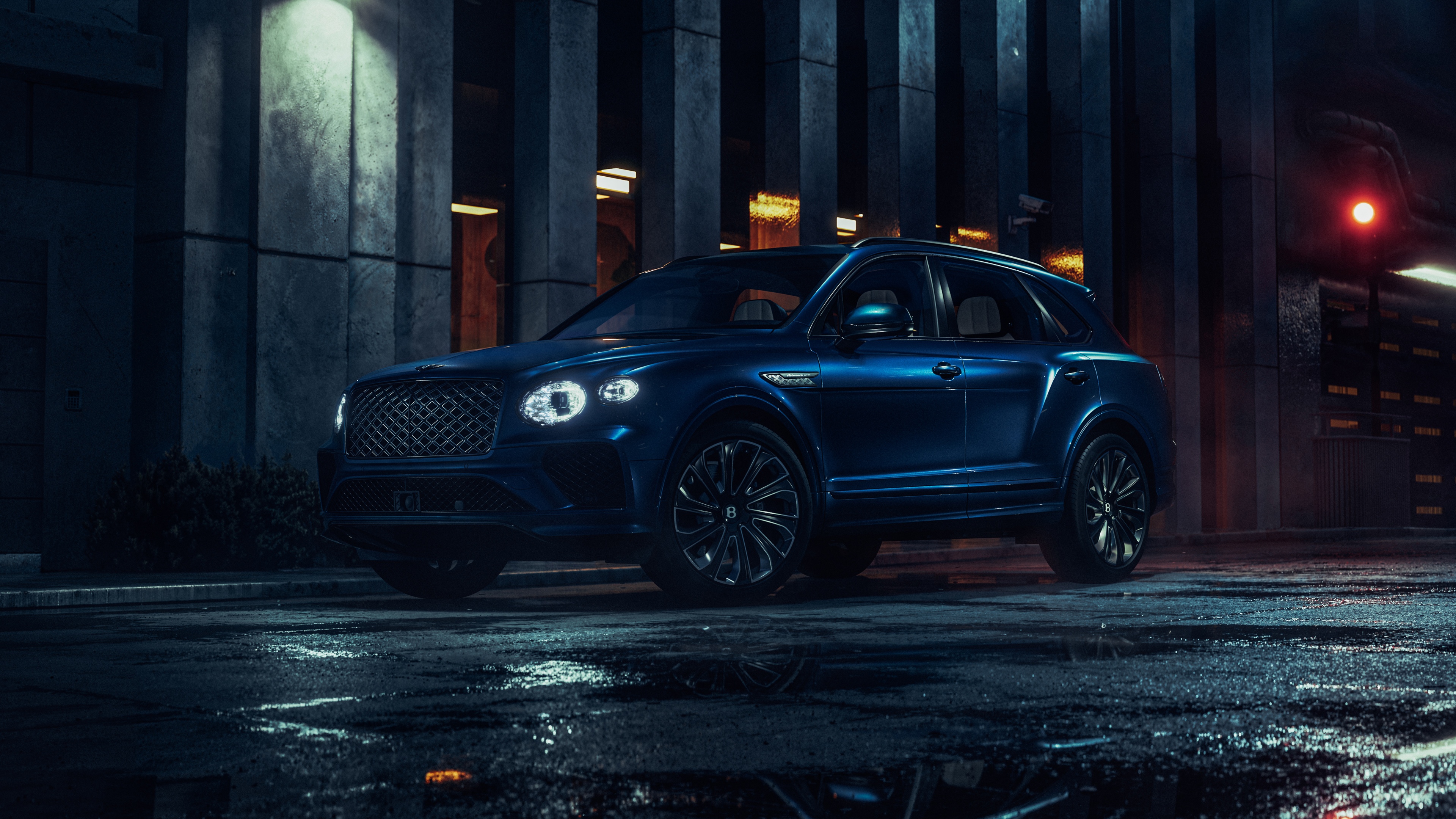 A 2026 Bentley Bentayga EWB driving through a dark urban street at night with city light reflections on its polished exterior.