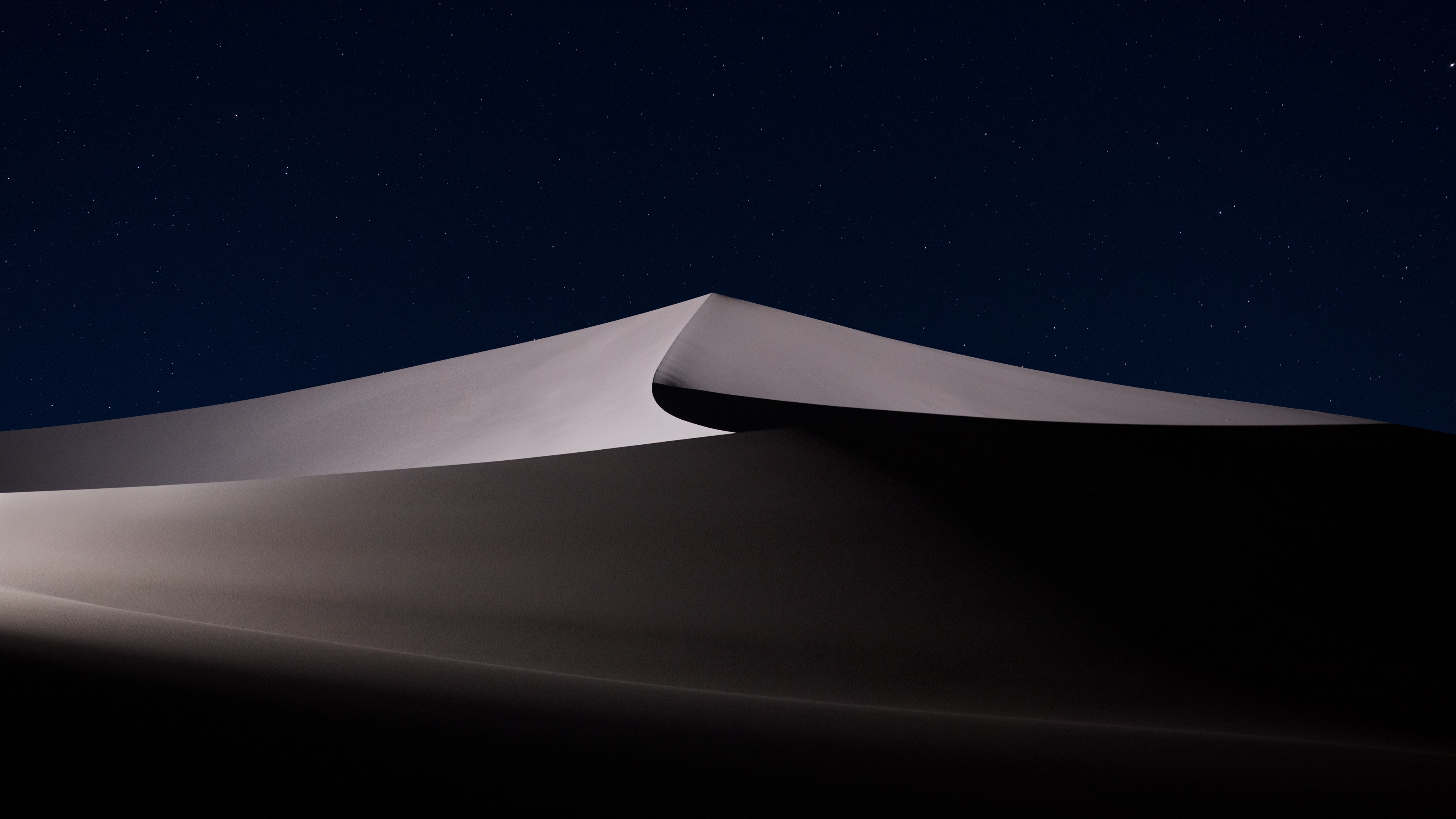 A vast desert landscape with rolling sand dunes beneath a dense, star-studded night sky.