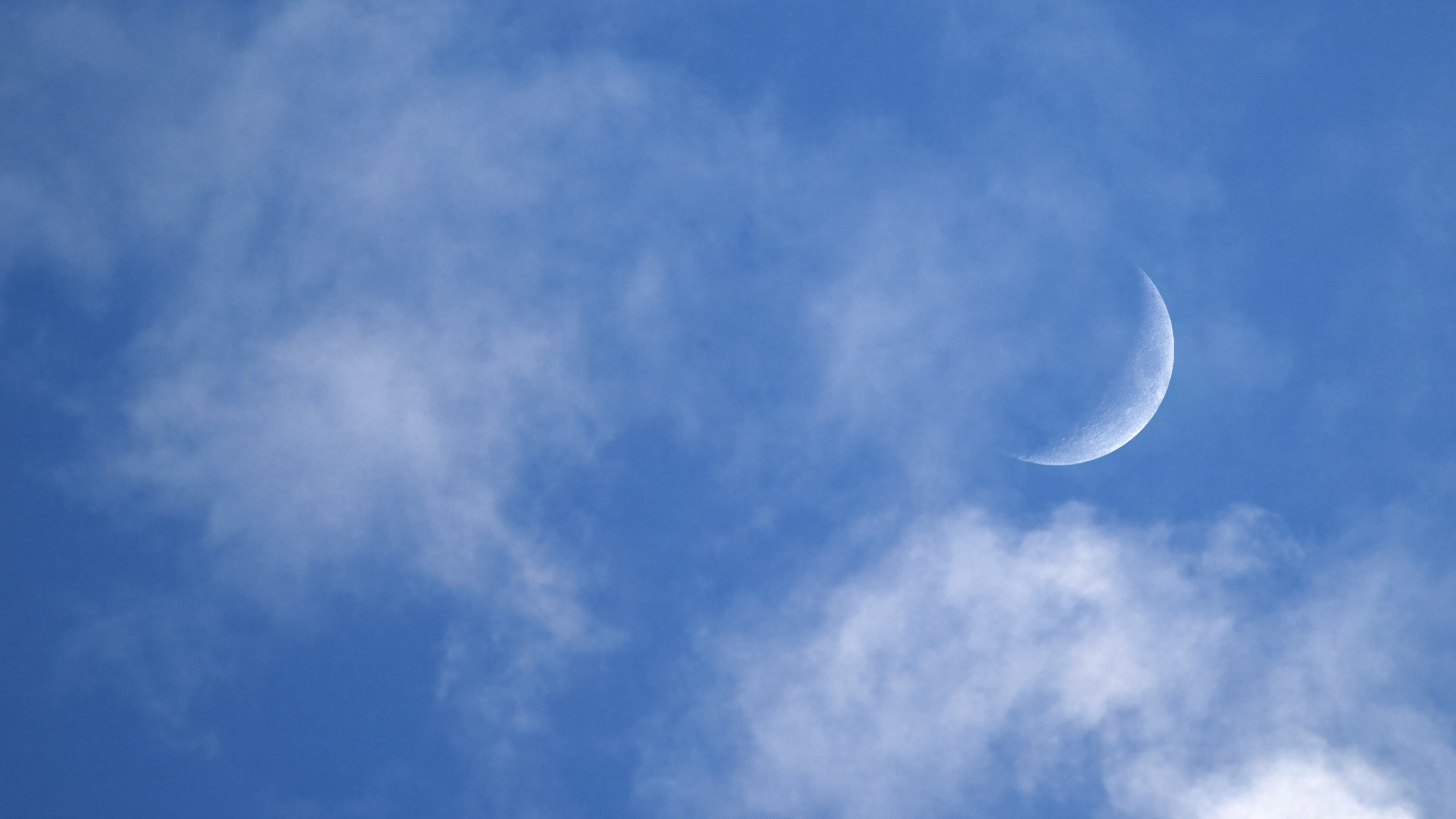 A luminous crescent moon shining through soft clouds in a deep blue night sky.