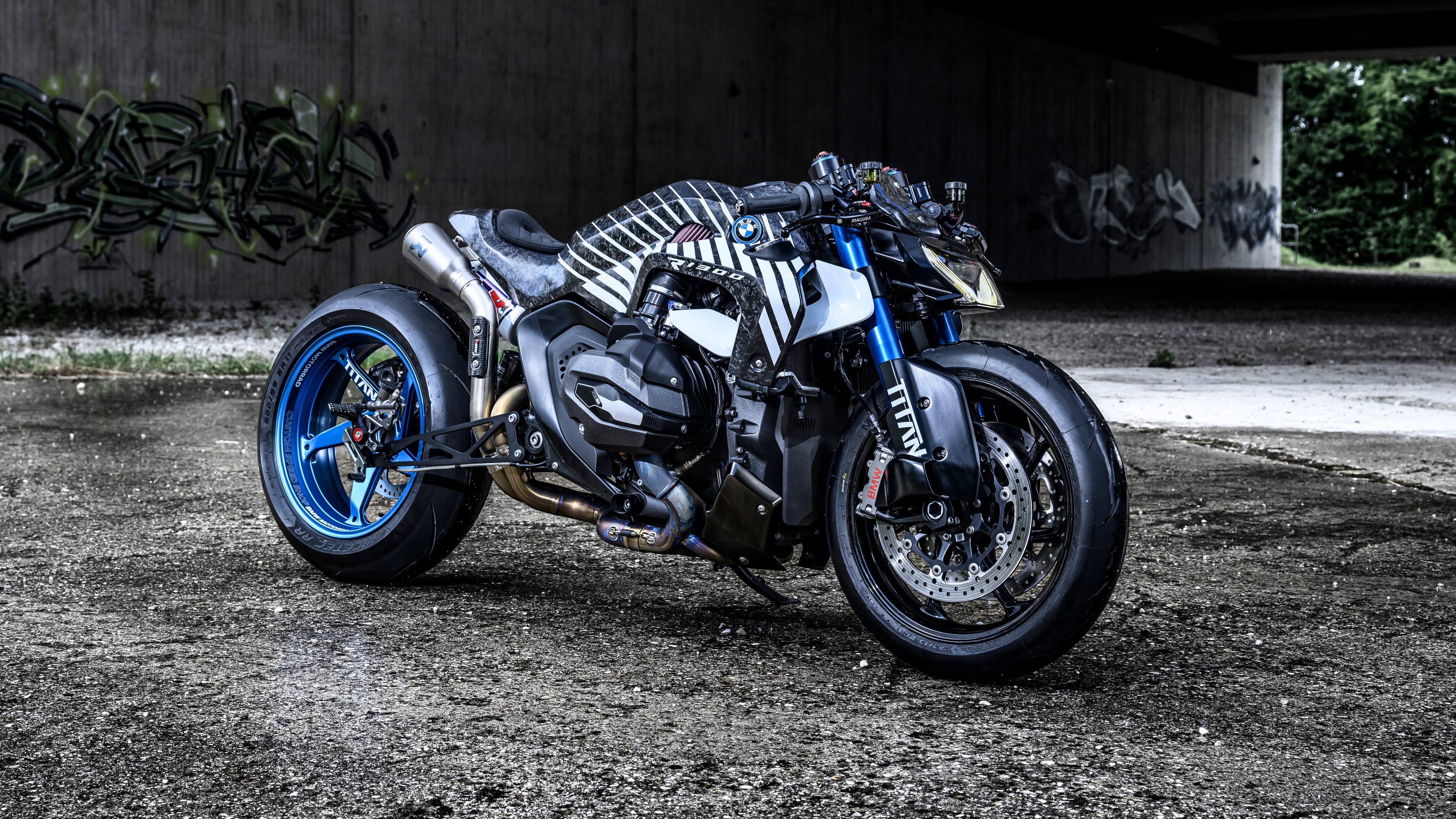 A custom BMW R 1300 R Titan motorcycle parked against a colorful graffiti wall in a city setting.