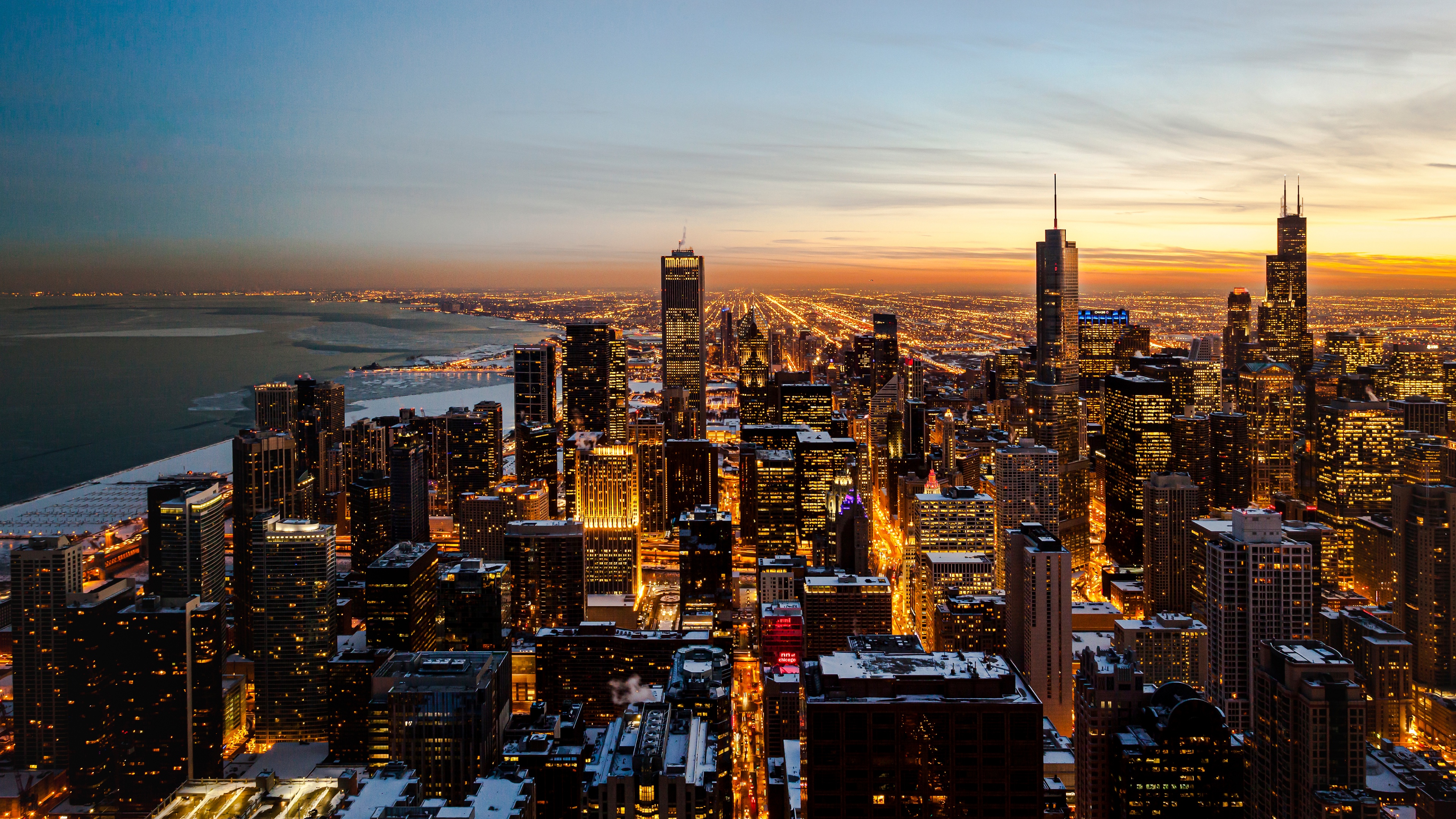 Aerial photography of the Chicago downtown skyline at sunset featuring skyscrapers and urban cityscape during dusk.