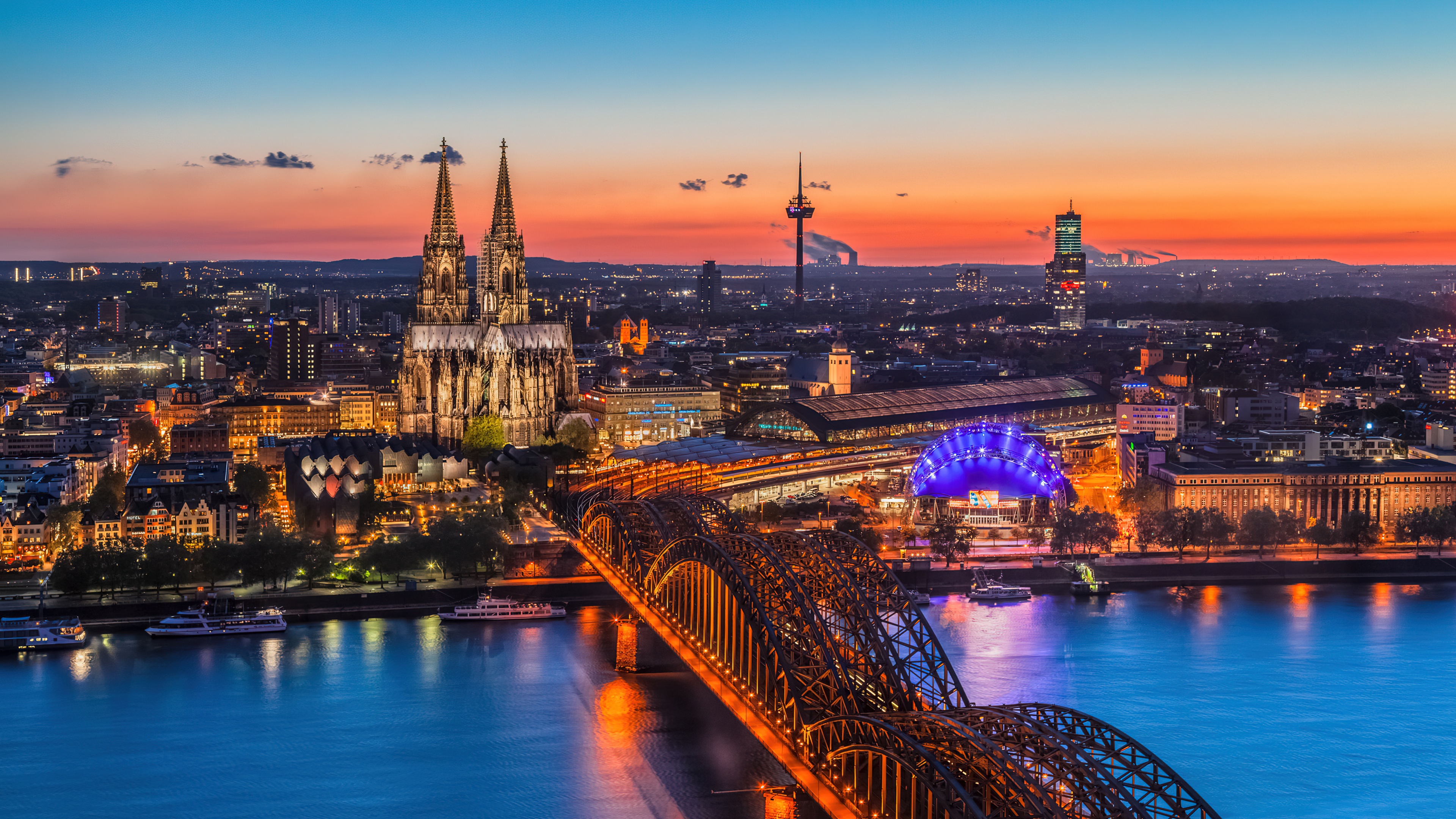A sunset cityscape of Cologne, Germany, featuring the Cologne Cathedral landmark.
