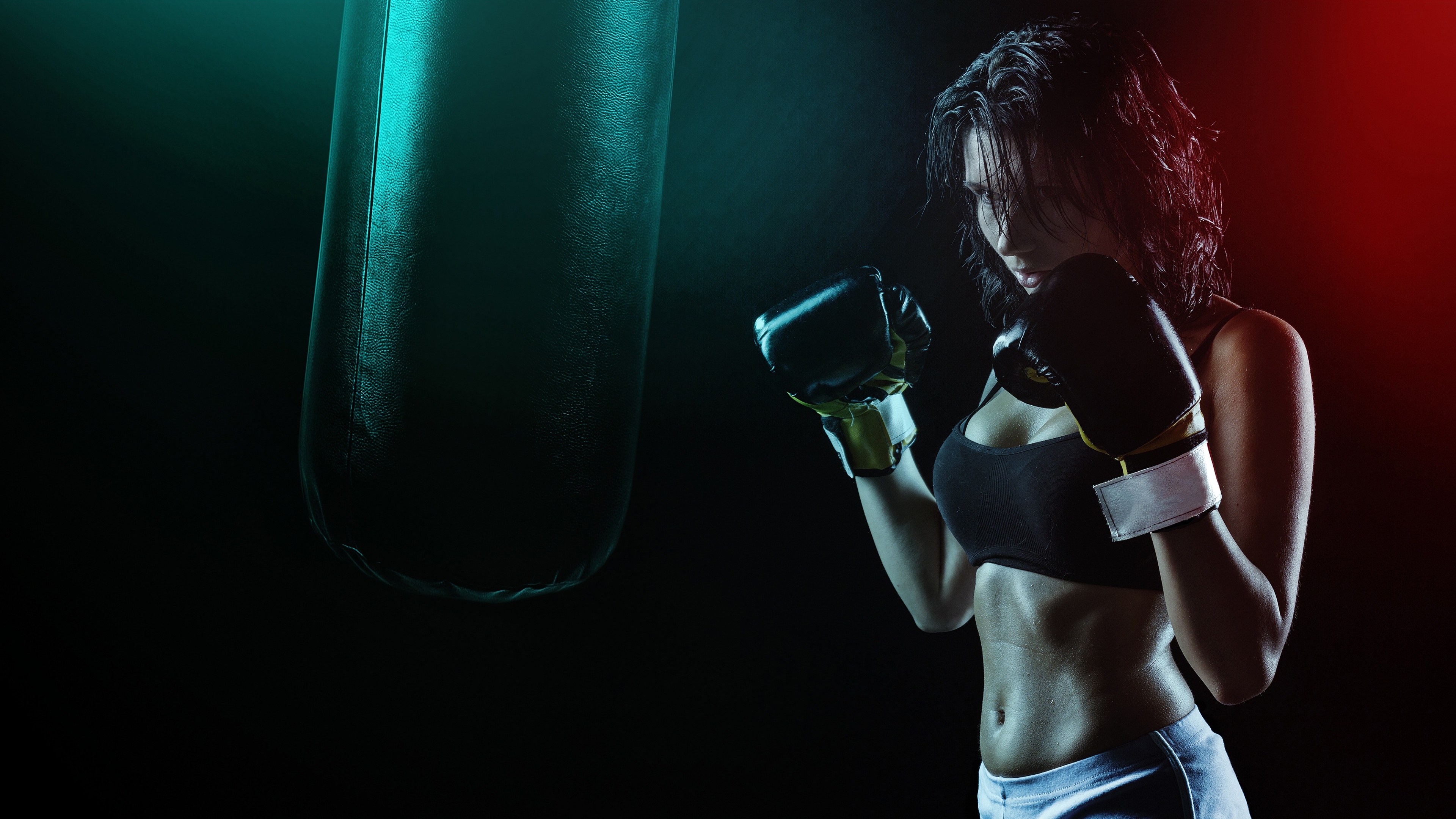 A close-up, dramatic portrait of a focused female boxer wearing boxing gloves against a dark, moody background.